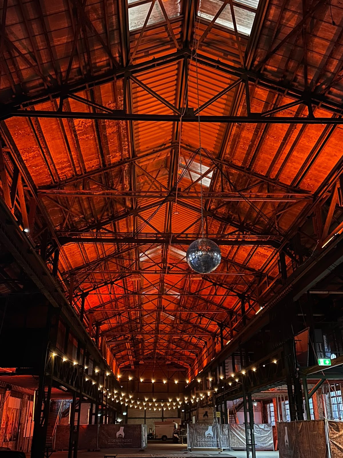 Blick in die hohe Stahlhalle der Zechenwerkstatt Lohberg mit warm beleuchtetem Dachstuhl, Discokugel und Lichterketten